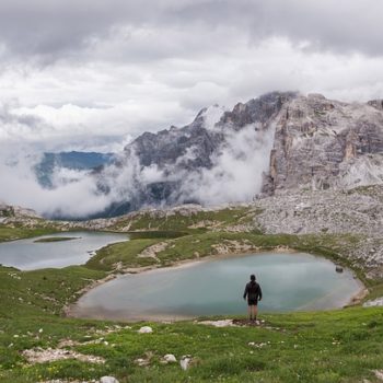 man standing in front of lake with mountains and clouds ahead