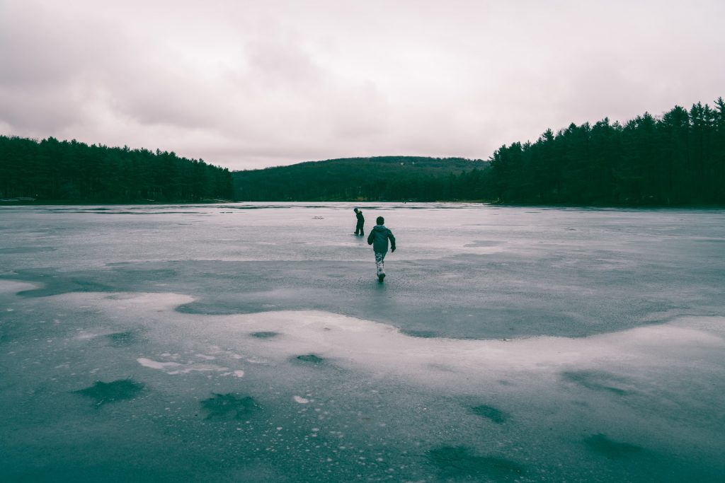 kids running on frozen lake with trees and hill in the background