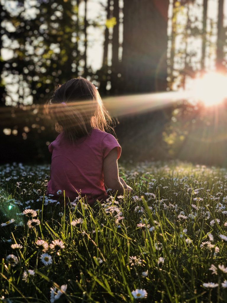 girl sitting in daisy flowerbed in forest with sunlight shining through