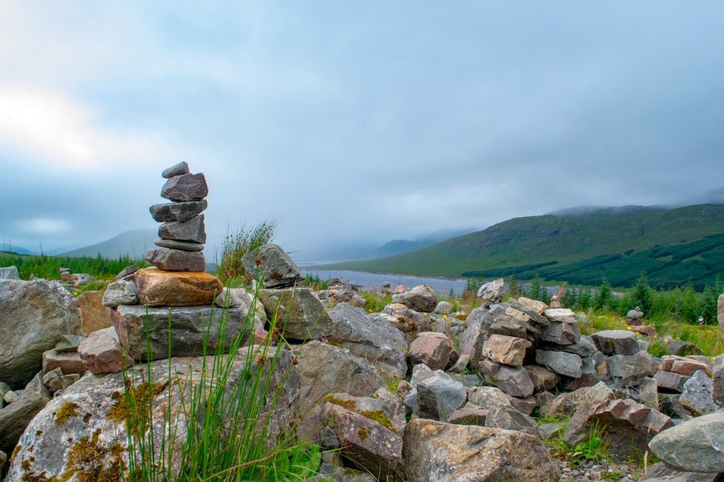 cairn overlooking a misty green hillside shrouded in clouds