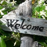 a wooden sign with the word welcome nestled in flowering foliage