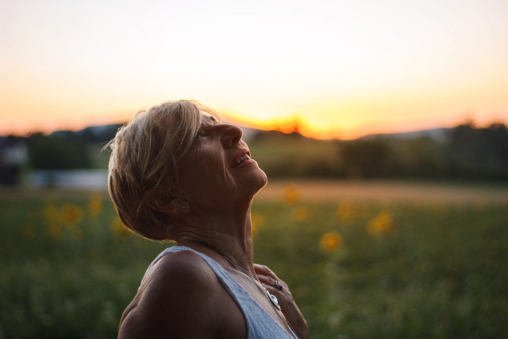 older woman with head tilted back looking up at the sky, with the sunset in the background